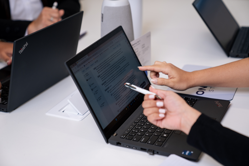 Two people collaborating at a table using Lenovo ThinkPad laptops, one pointing at the screen and the other holding a pen.