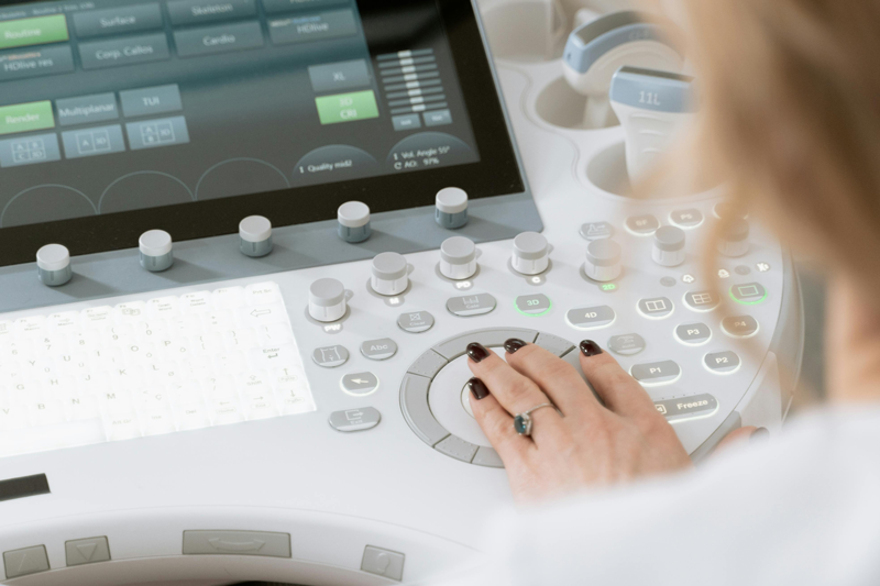 Close-up of a person operating controls on a medical ultrasound machine with a touchscreen display and multiple buttons.