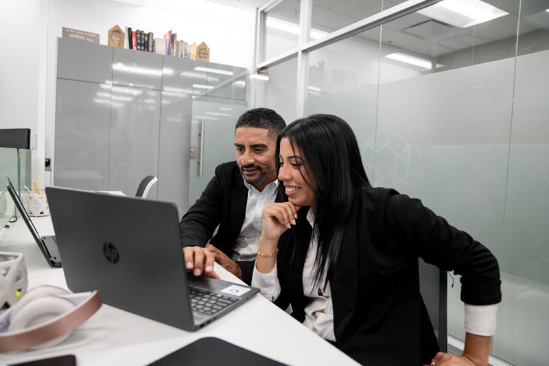 Two business colleagues smiling and looking at a laptop screen together in a modern office.