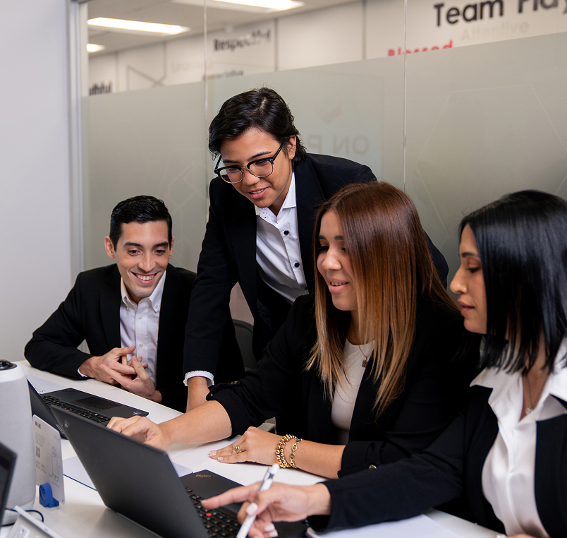 Four diverse business professionals collaborating around laptops in a modern office.
