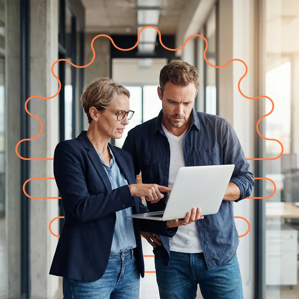 White collar executives talking in the office hallway looking at a laptop