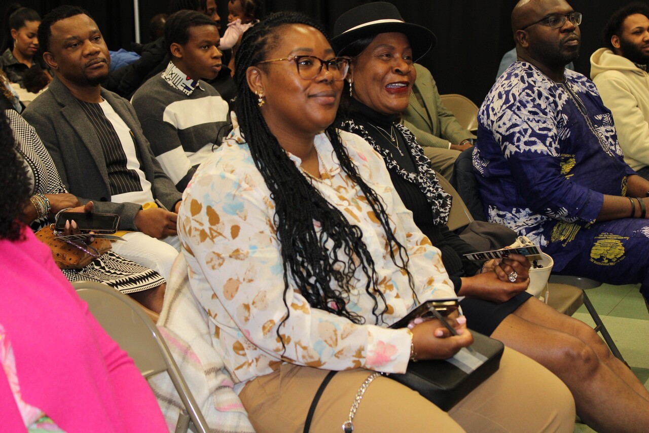 A group of diverse adults sitting closely together in folding chairs, attentively watching an event.
