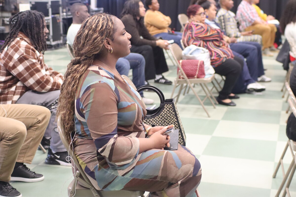 People seated in rows on folding chairs in a well-lit indoor setting, attentively facing forward.