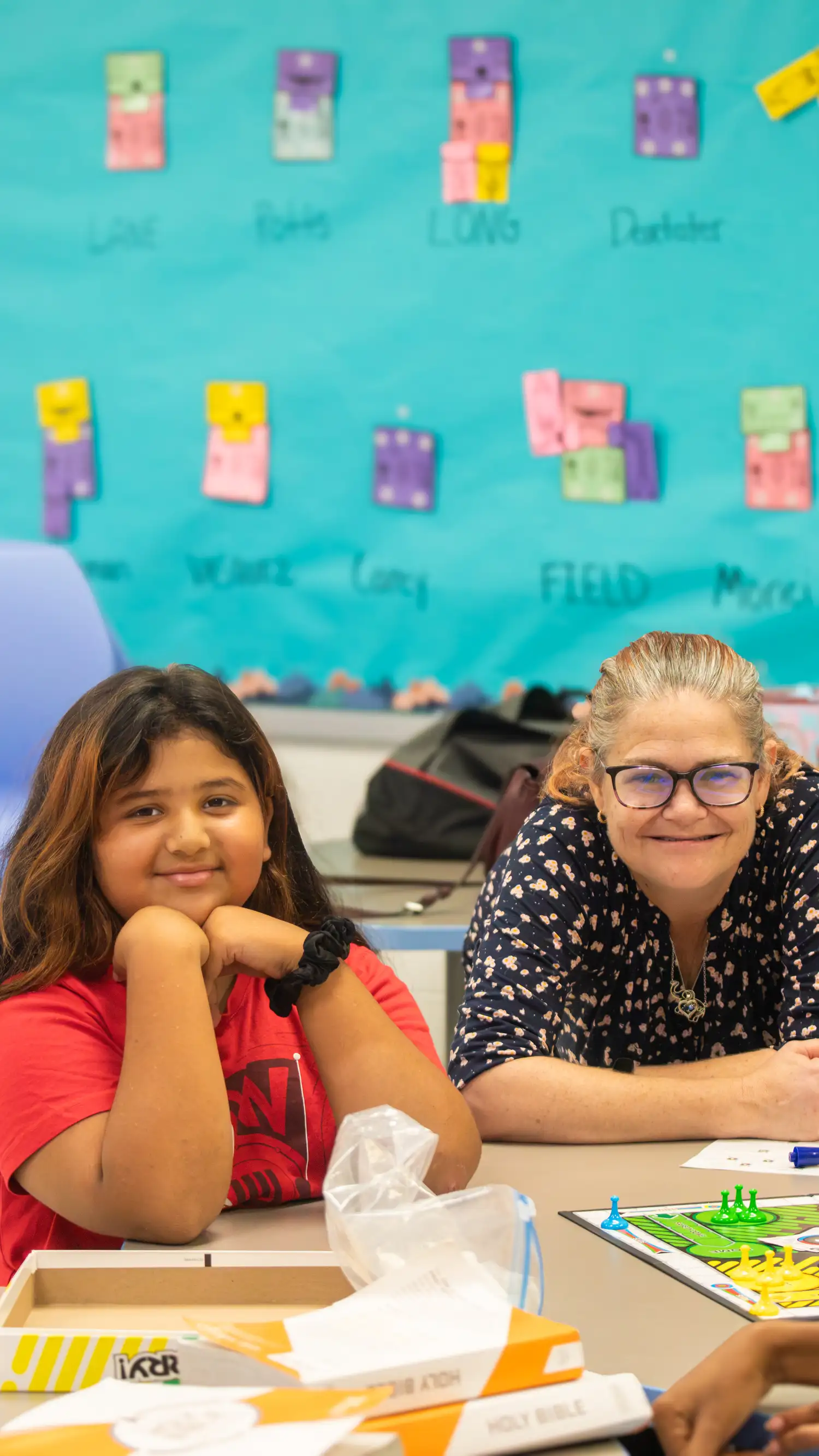 Girl and volunteer smiling at a table with a board game and Bibles in the kids classroom at Restoration Church in Laurel, Maryland