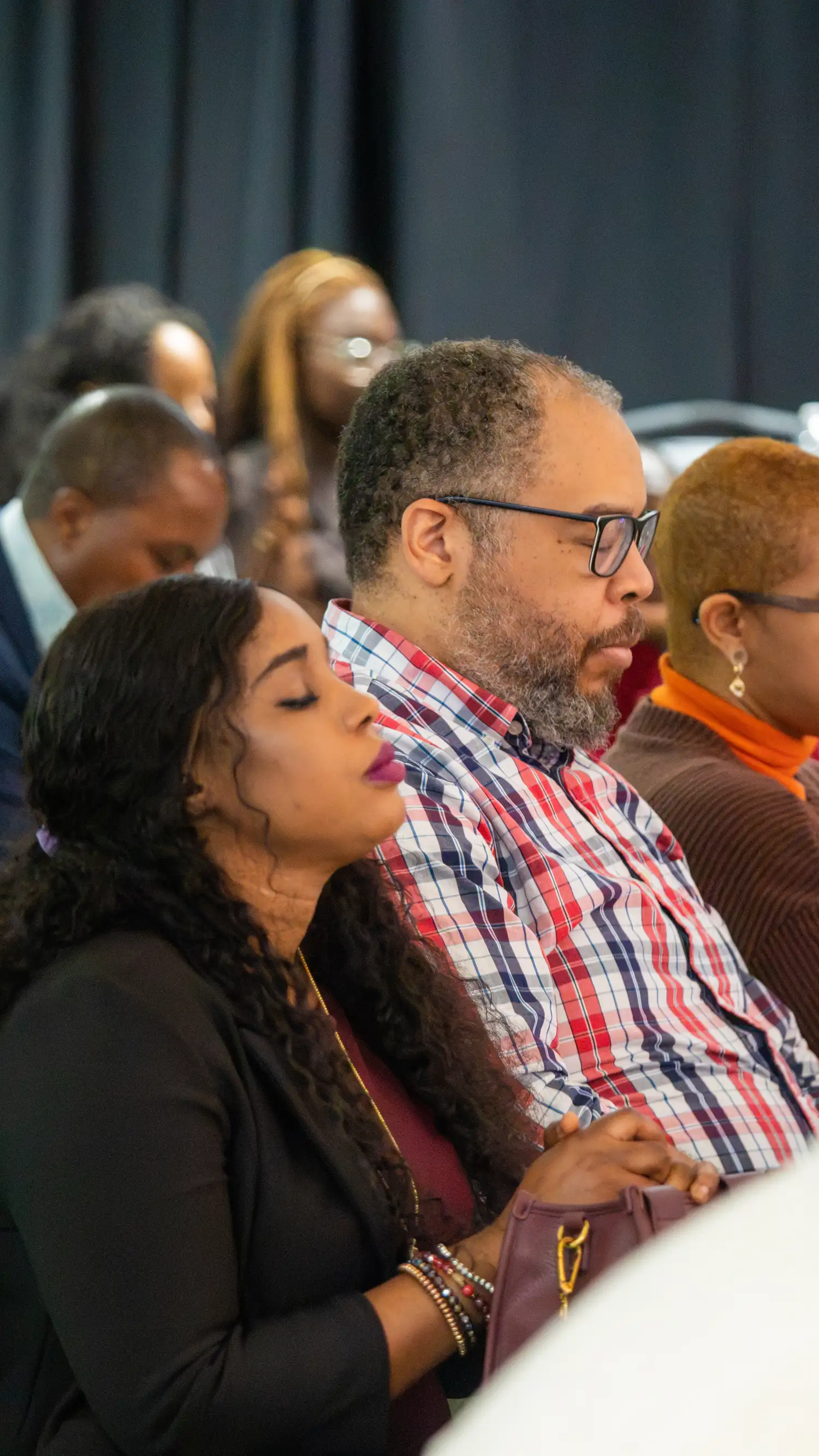 Congregation members with eyes closed in prayer during worship at Restoration Church in Laurel, Maryland
