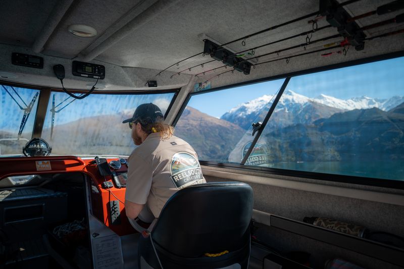 Reel South Charters skipper at the helm with snow-capped peaks ahead