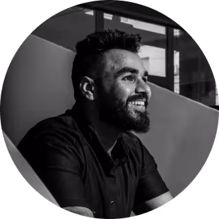 Black and white image of a smiling man with a beard and short hair sitting indoors.
