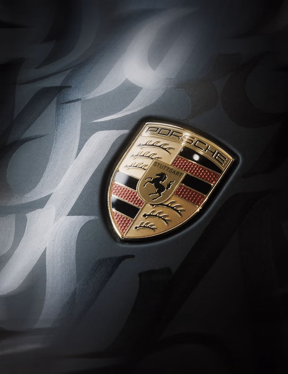 Nahaufnahme des Porsche-Wappens auf dunkelgrauem Hintergrund mit abstrakten Mustern.