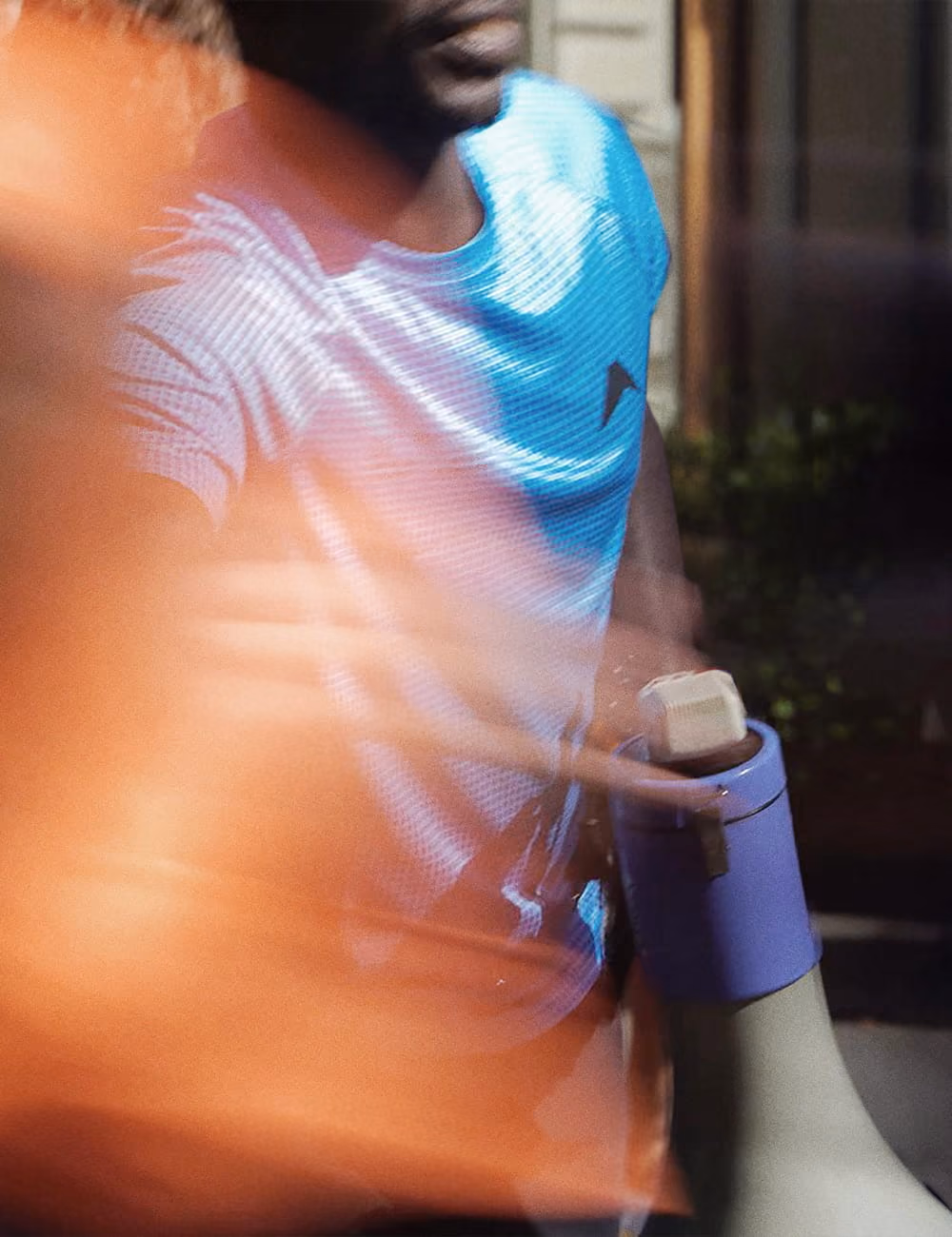 Mann in blauem Shirt hält ein Megafon in der Hand, unscharfe orange Unschärfe im Vordergrund.