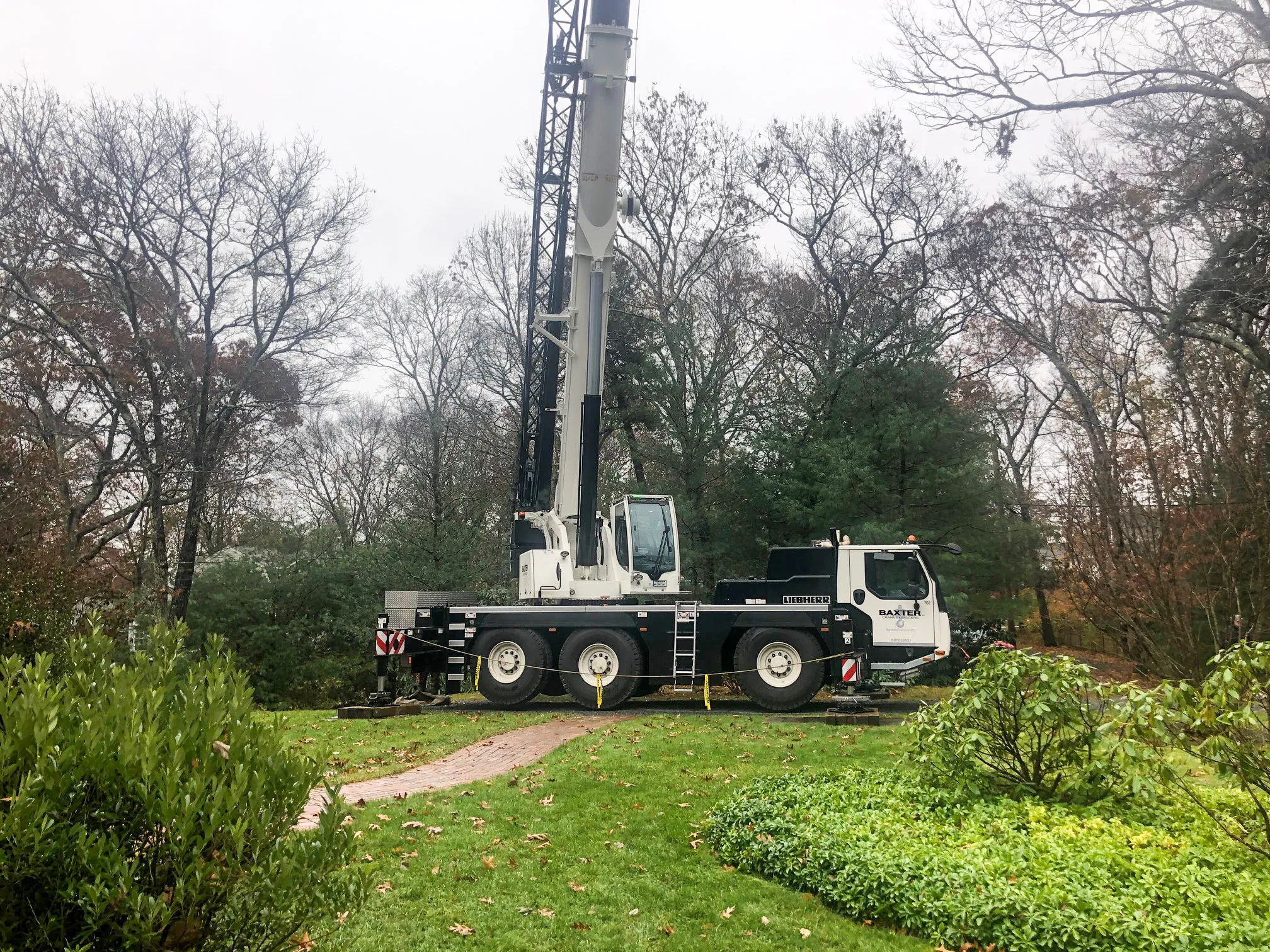 Liebherr mobile crane with extended boom positioned on green grass surrounded by trees in a park-like setting.