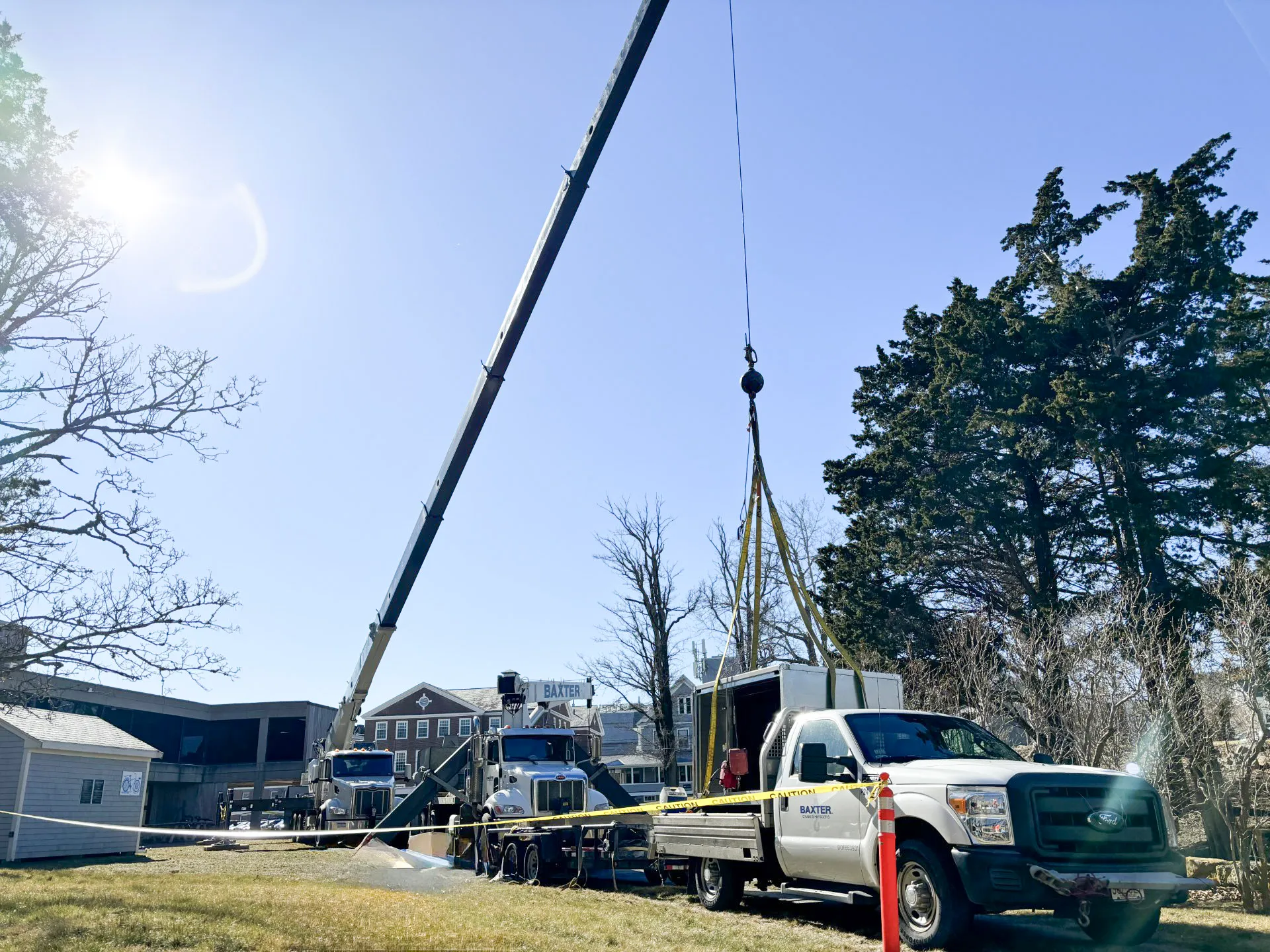 A crane truck lifting equipment near a white Ford pickup truck with caution tape around the work area on a sunny day.