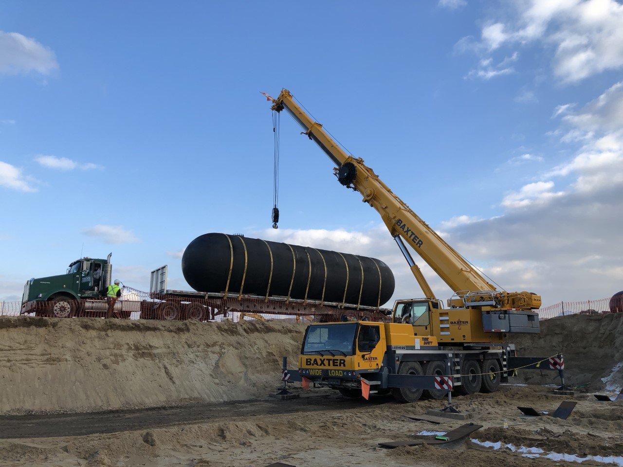 Baxter Crane lowering large underground tank into excavated pit during civil infrastructure project