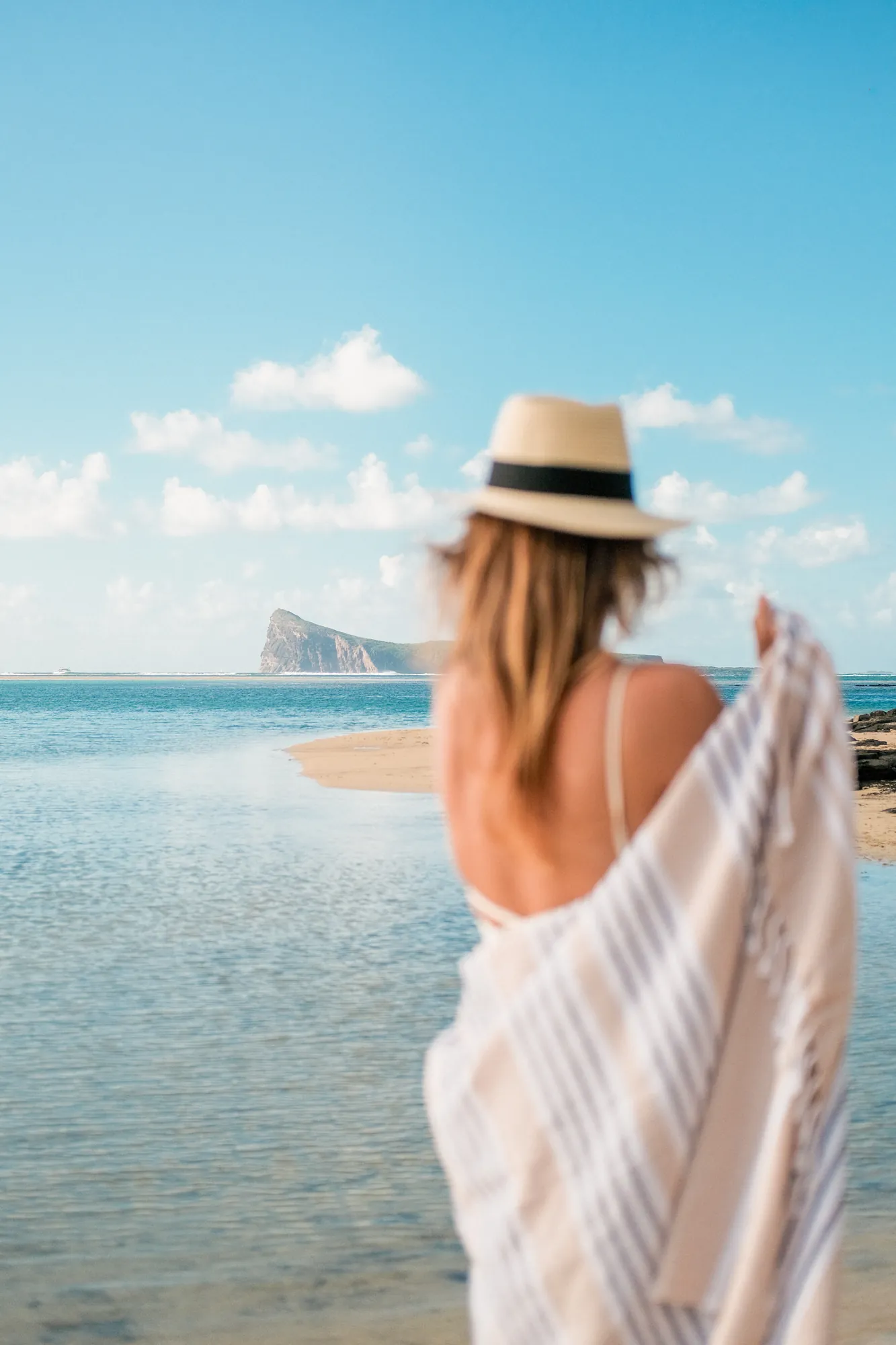 Femme au chapeau de paille drapée d'une serviette rayée, face au lagon