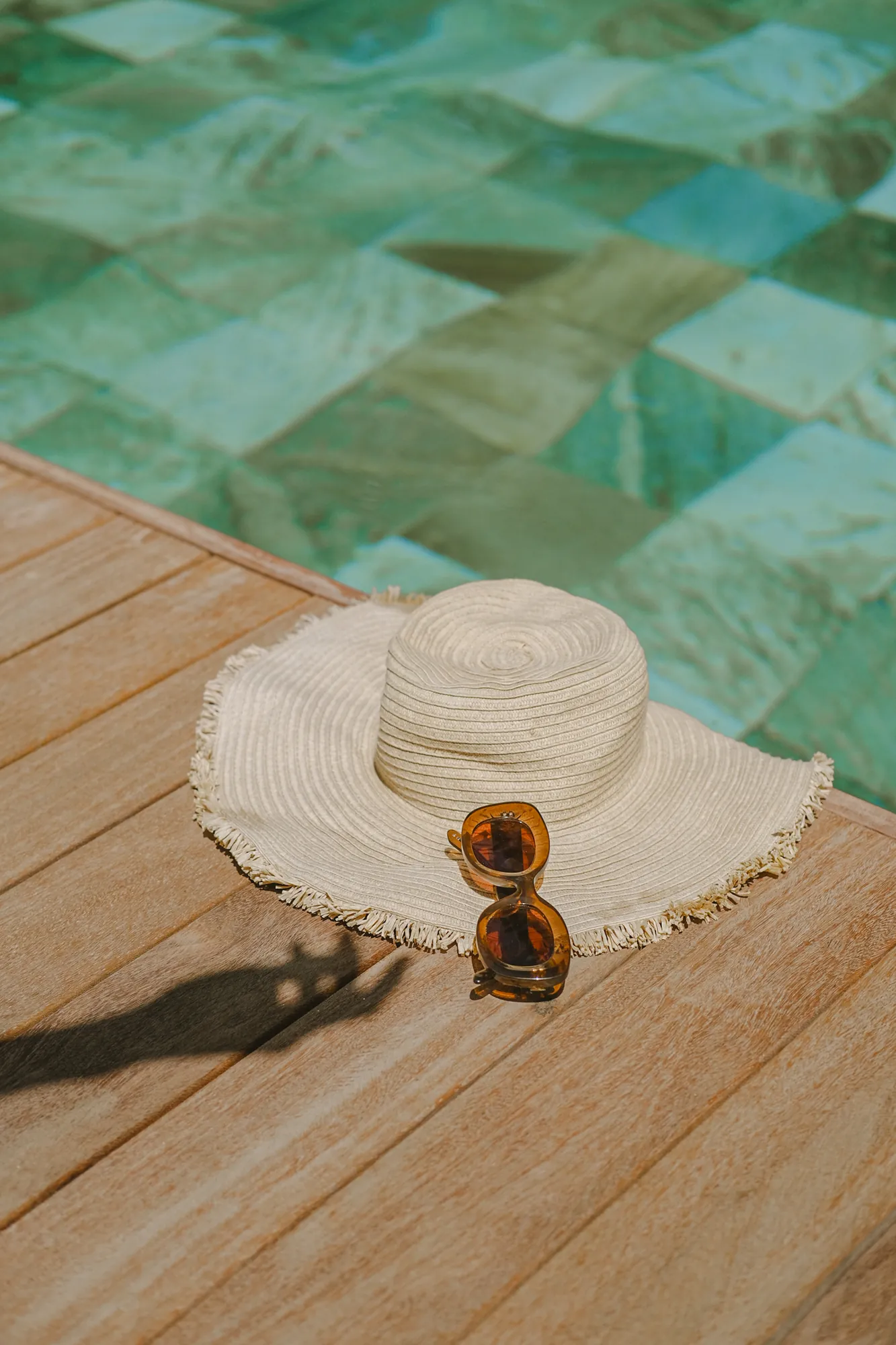 Chapeau de paille et lunettes de soleil posés au bord d'une piscine