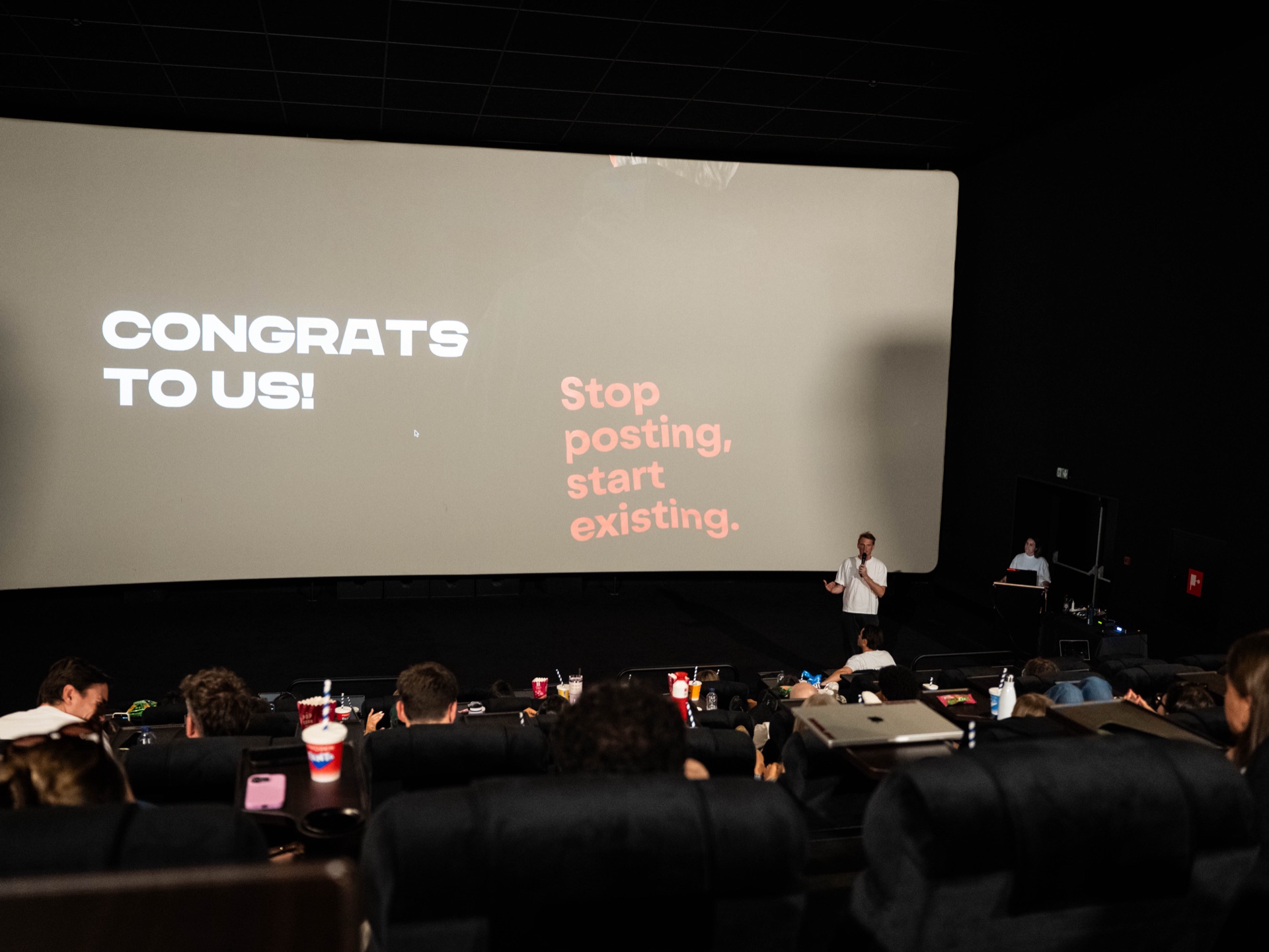 Bioscoopscherm met « Congrats to us! » en de socialsky-tagline « Stop posting, start existing. »