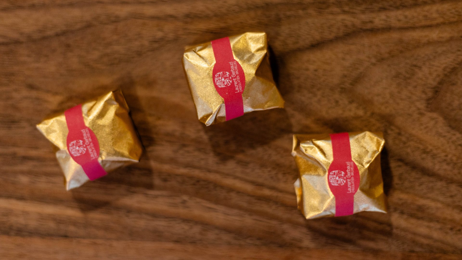 Three Laurent Gerbaud pralines in gold and red wrapping on a wooden table