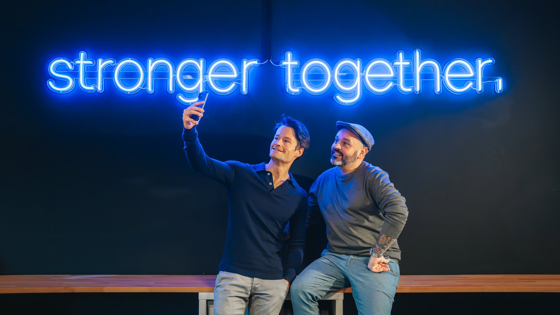 Deux membres de l'équipe Overloop font un selfie sous un néon « stronger together »