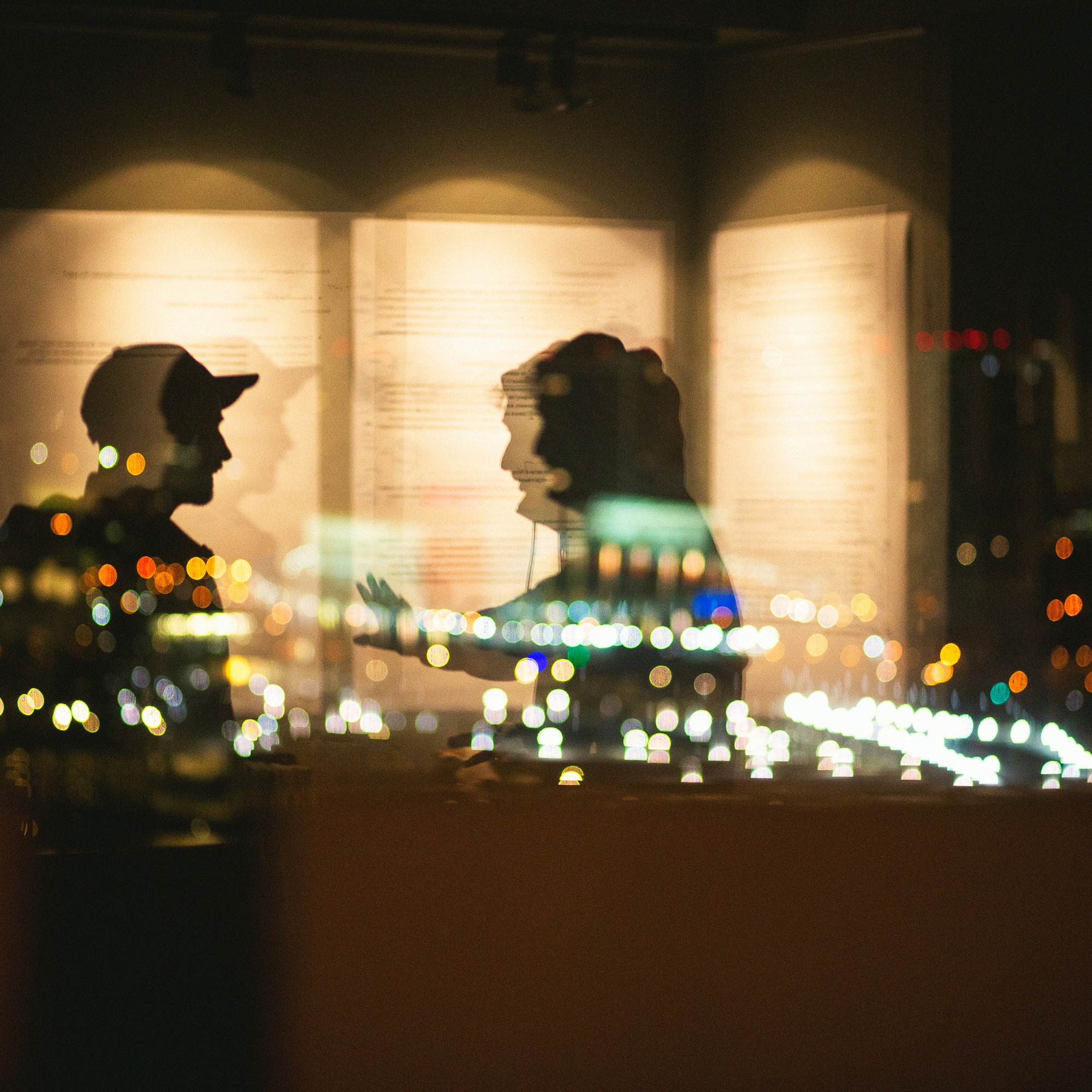 Silhouetten von zwei Personen, die sich vor beleuchteten Informationswänden unterhalten, mit verschwommenen Stadtlichtern im Vordergrund.