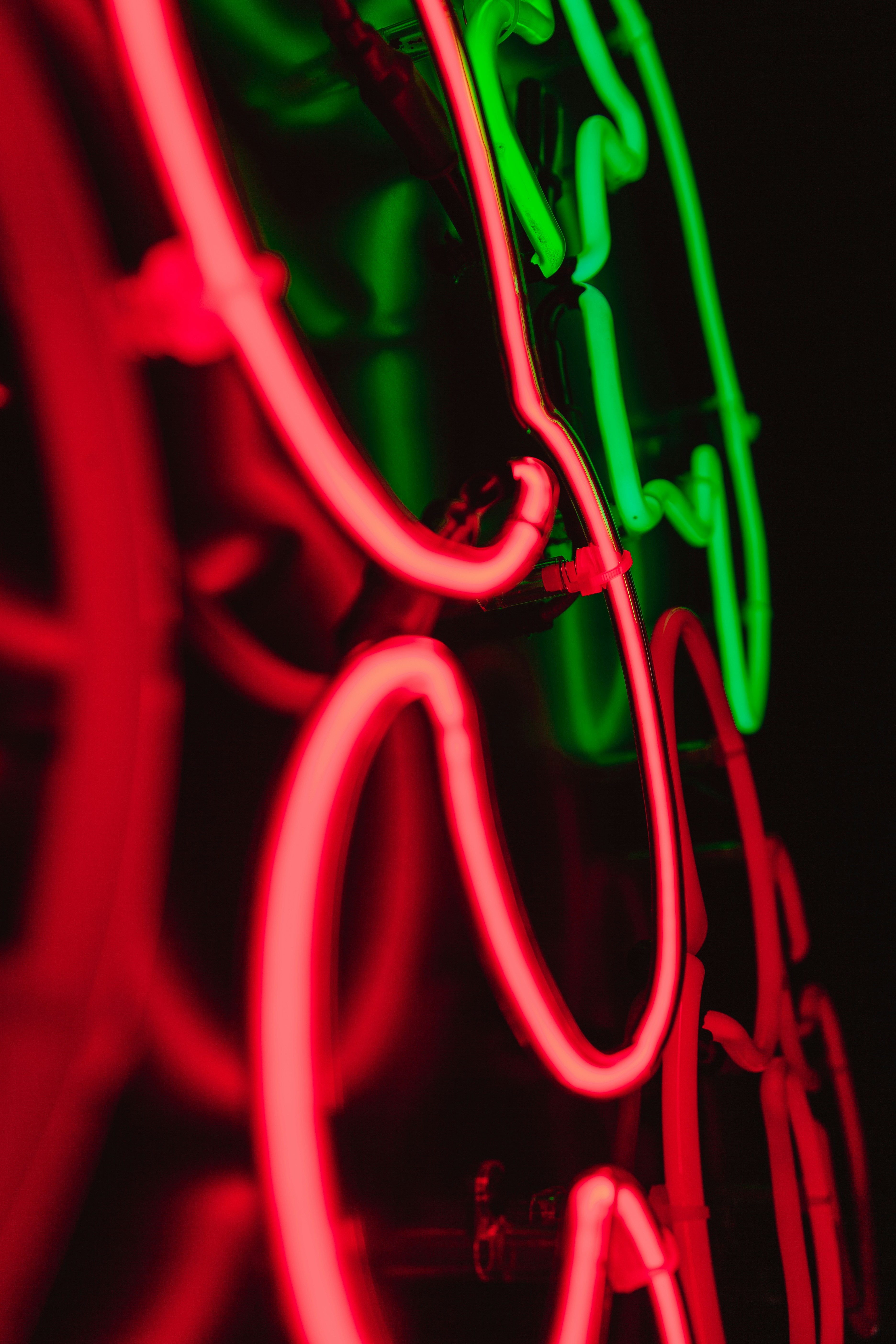 Nahaufnahme von roten und grünen leuchtenden Neonröhren vor schwarzem Hintergrund.