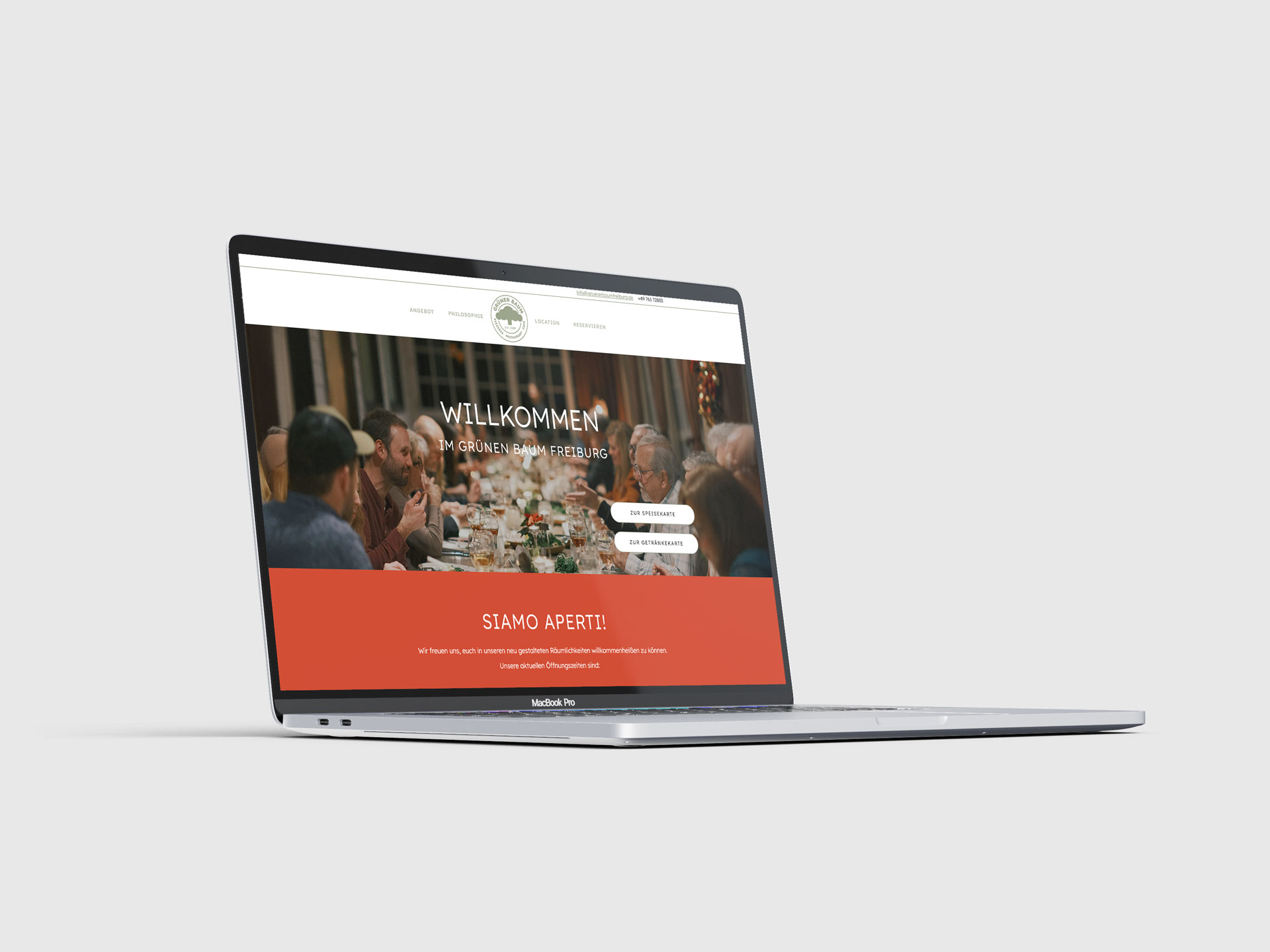 MacBook Pro zeigt die Webseite des Grünen Baum Freiburg mit einem Bild von Menschen bei einem gemeinsamen Essen und einer Willkommensnachricht.