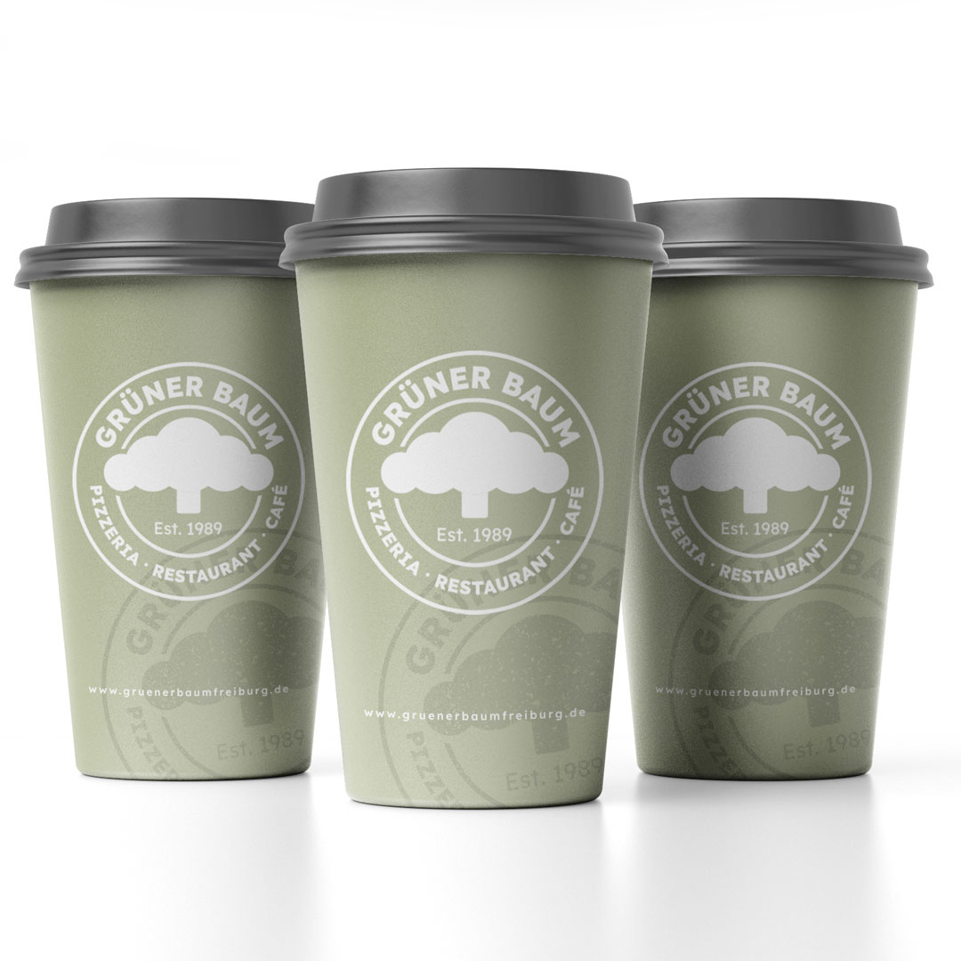 Drei grüne Einweg-Kaffeebecher mit schwarzem Deckel und weißem Logo von Grüner Baum Pizzeria, Restaurant, Café.