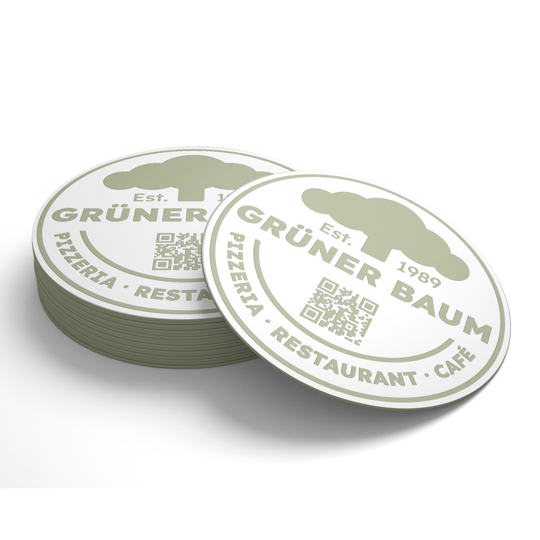Gestapelte runde Bierdeckel mit dem Logo von Grüner Baum, Pizzeria, Restaurant und Café, inklusive QR-Code.