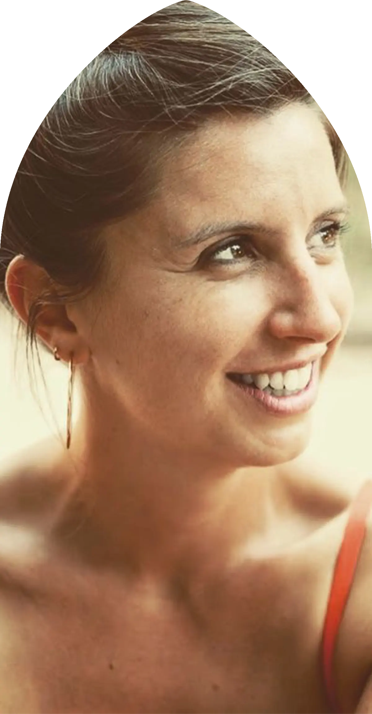 Portrait d'une femme souriante regardant vers la droite, portant des boucles d'oreilles et une robe à bretelles fines rouge.