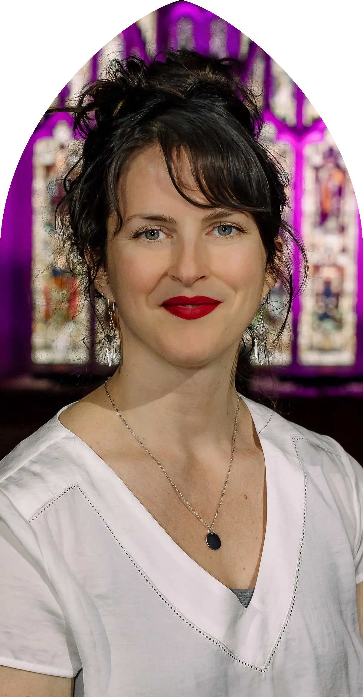 Portrait d'une femme aux cheveux bruns bouclés, portant un haut blanc et un collier avec un pendentif noir, avec un arrière-plan flou lumineux violet.