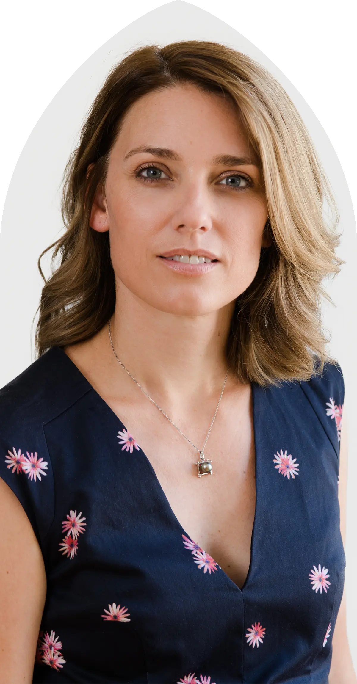 Femme aux cheveux bruns mi-longs portant une robe bleu marine avec des motifs floraux roses et un collier argenté.