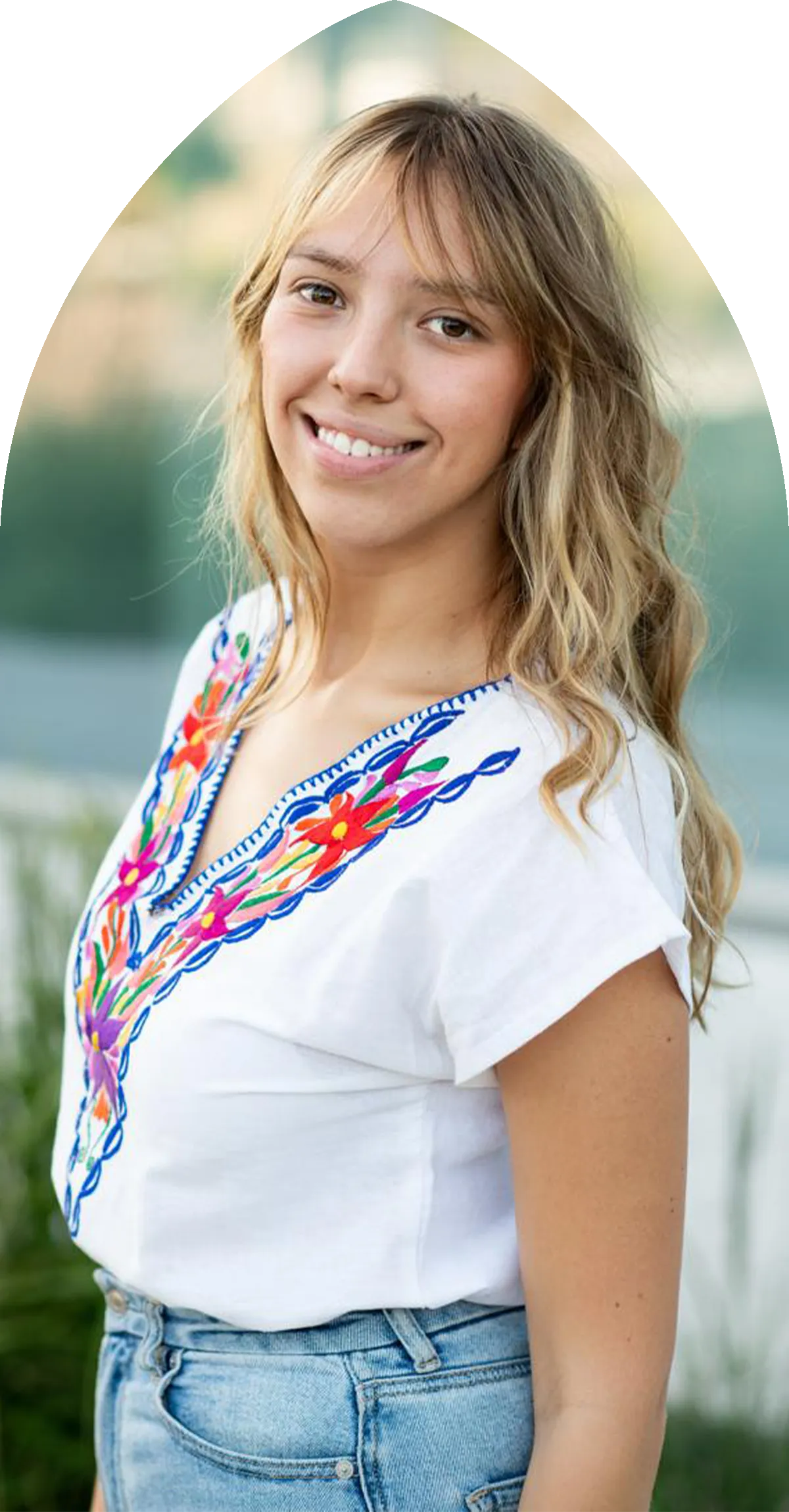 Femme aux cheveux bruns mi-longs portant une robe bleu marine avec des motifs floraux roses et un collier argenté.