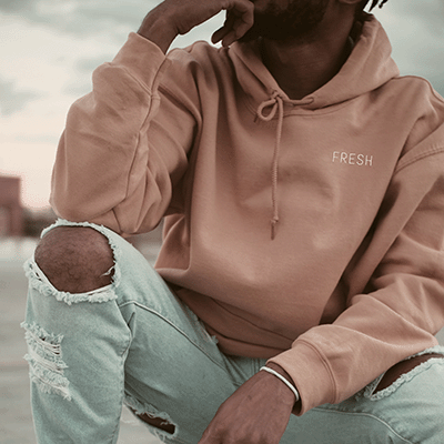 A man wearing a peach-coloured hooded sweatshirt with the word "fresh" embroidered on the chest
