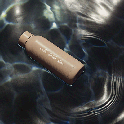 A high-quality reusable water bottle with the words "Well, hello there" floating on reflective water