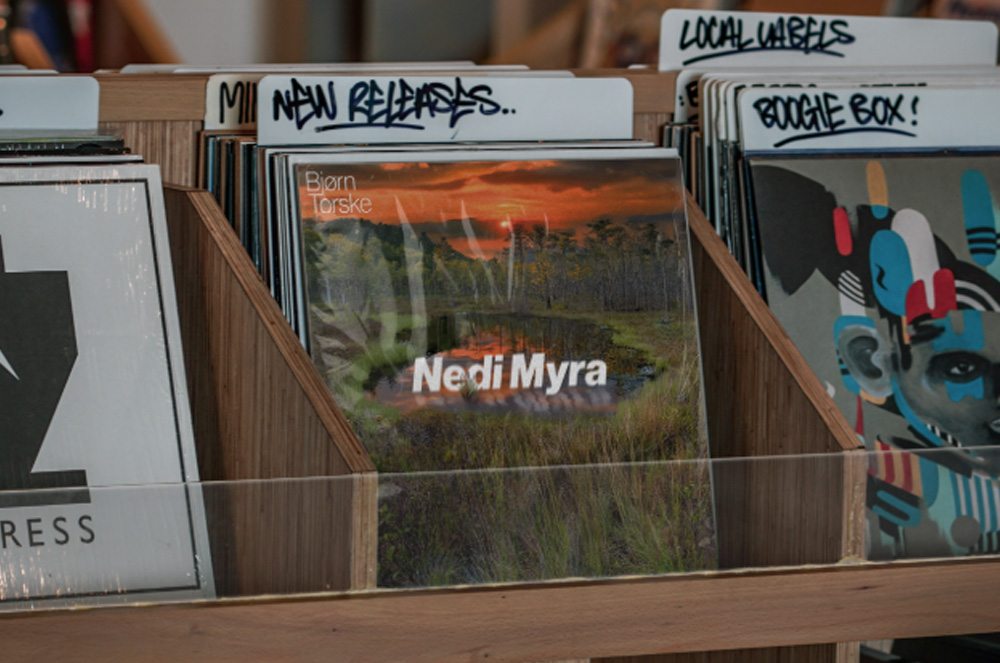 Mockup av vinylcoveret stående i en hylle i en platebutikk.