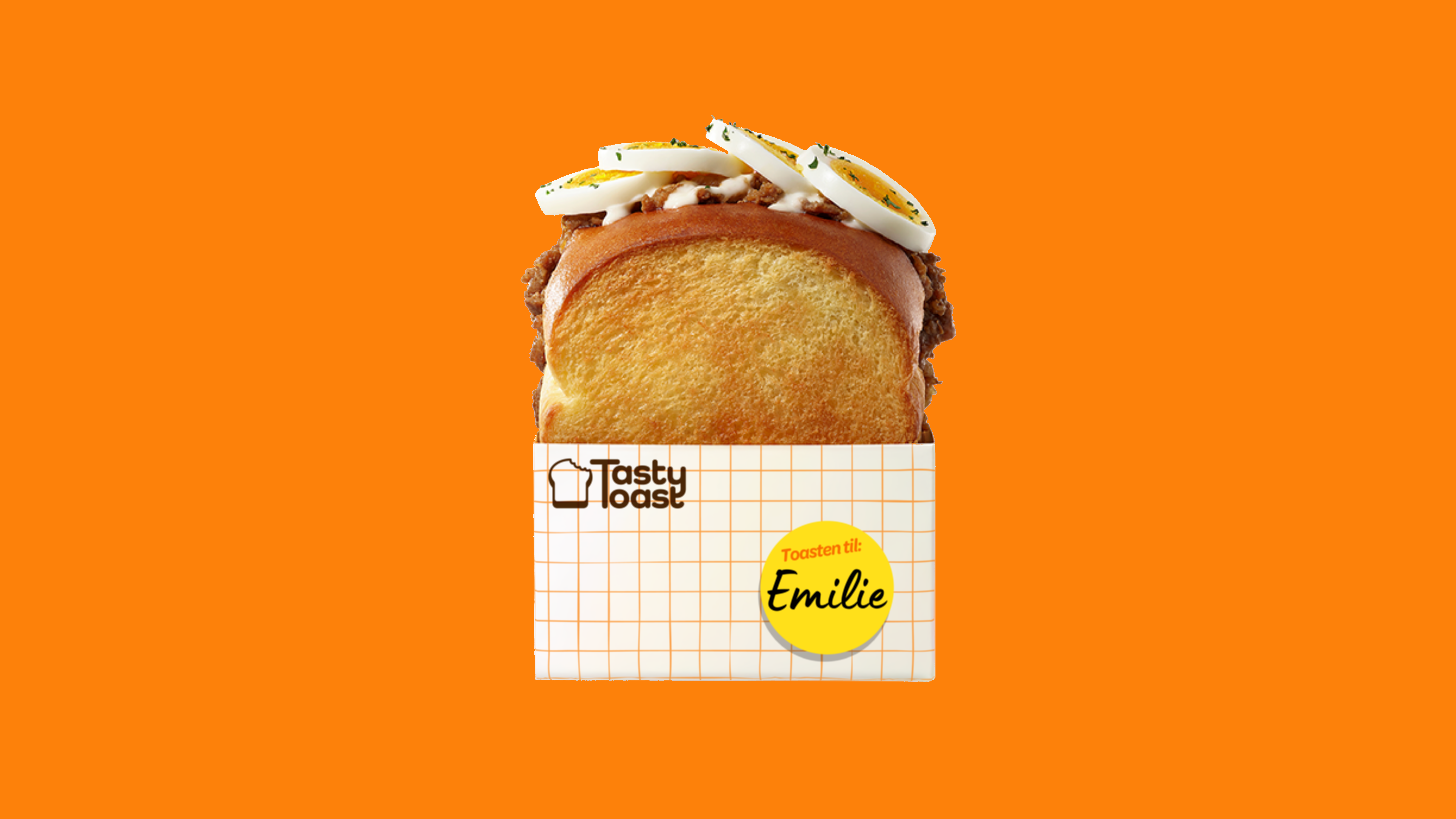 Toasted sandwich with ground meat, sauce, and sliced boiled eggs on top in branded packaging.