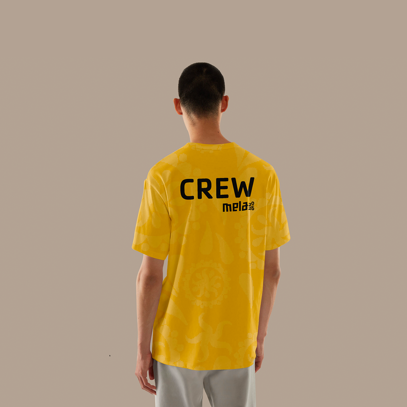 Person wearing a yellow crew t-shirt with floral patterns and 'CREW mela 2026' text on back.
