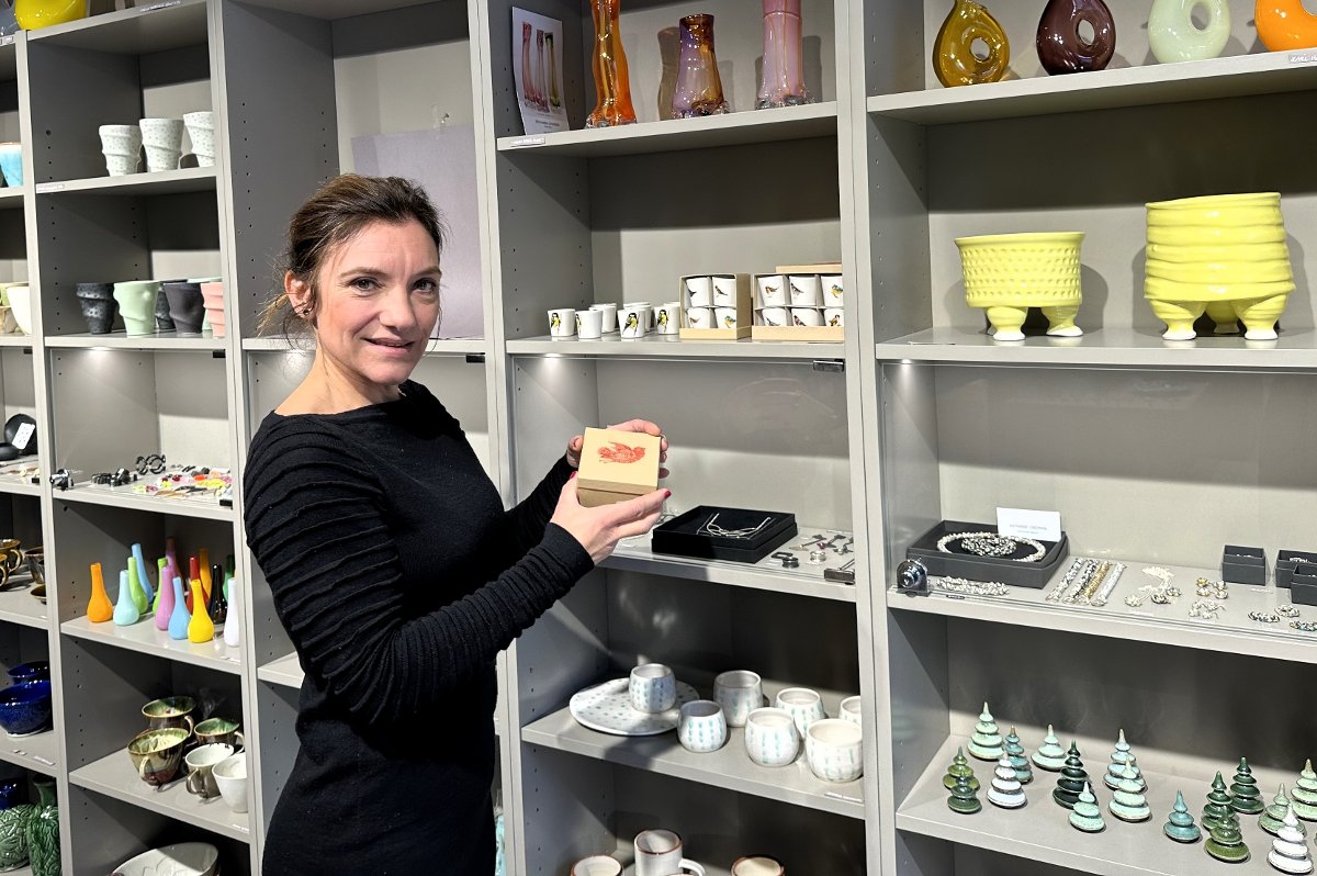 Woman in black holding a small box in a shop with shelves of colorful ceramics and jewelry.