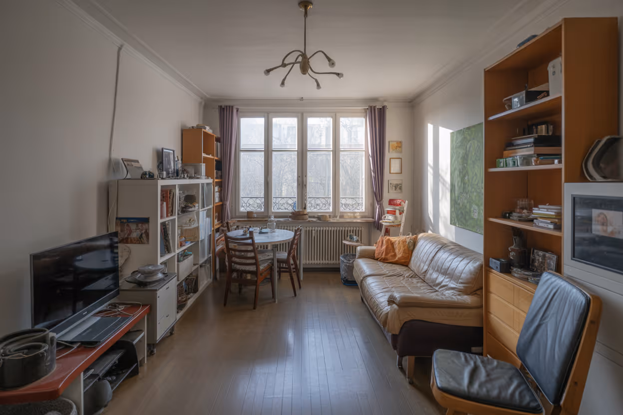 Wohnzimmer mit brauner Ledercouch, Holztisch mit Stühlen vor großen Fenstern und Regalen mit Büchern und Dekoration vor einer Haushaltsauflösung