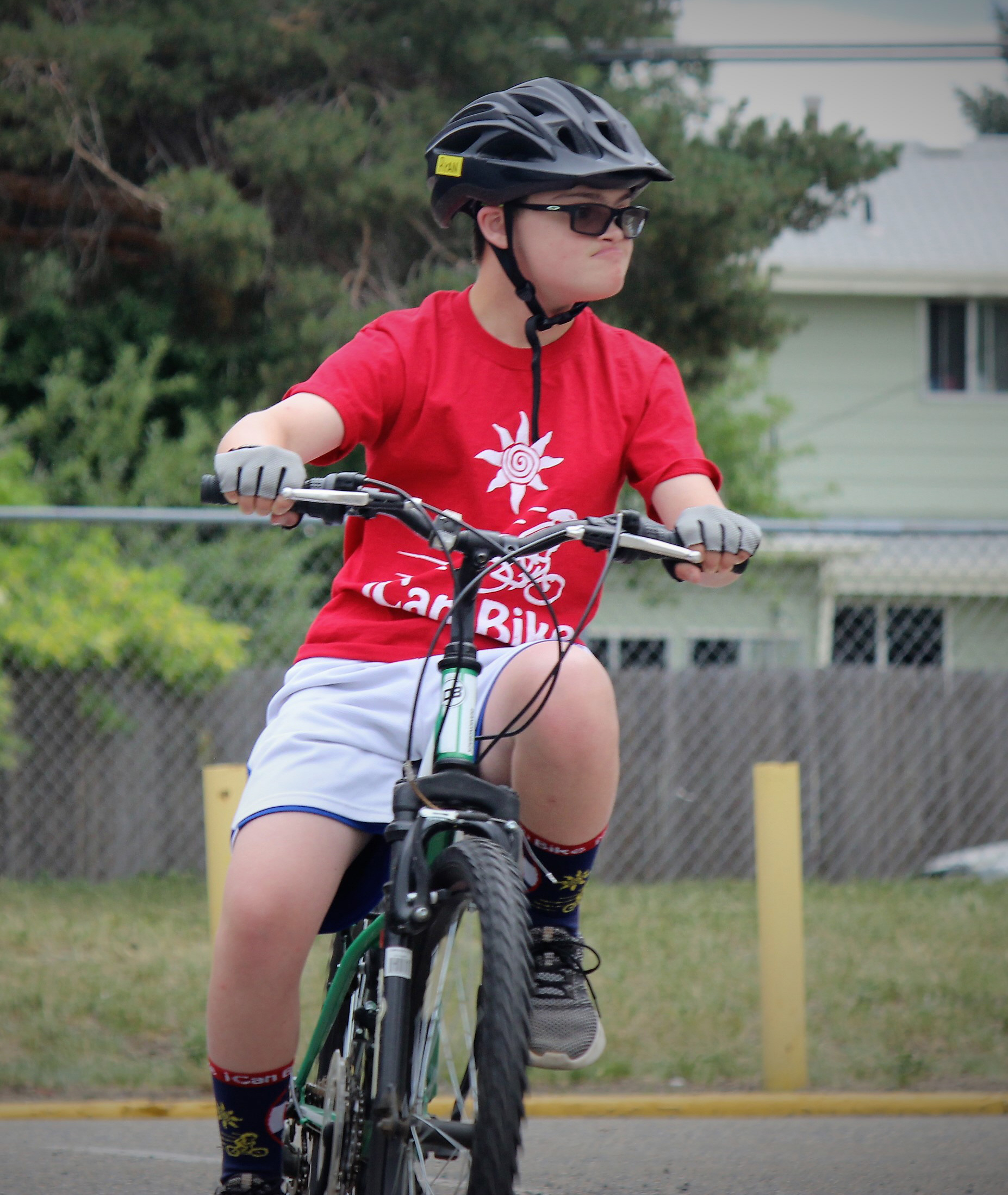 Child with a disability wearing a red iCan Bike shirt and bicycle helmet riding a bike on a track during Cycle Movement's adaptive cycling camp in Colorado