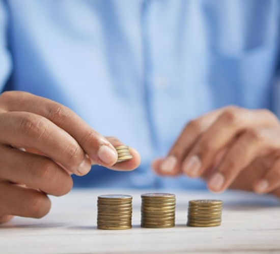 Person stacking three ascending piles of coins on a table, symbolizing saving or financial growth.