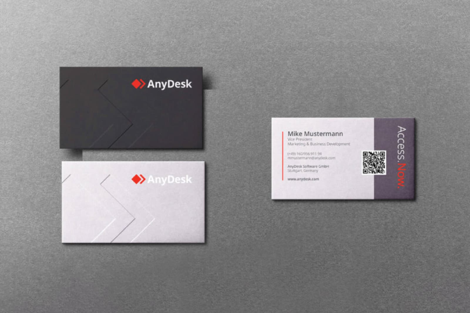 Three AnyDesk business cards on a gray surface; two show the company logo on black and white backgrounds, one shows contact details for Mike Mustermann with a QR code and the phrase 'Access. Now.'