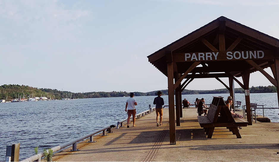 Aerial view of a snowy landscape with a frozen lake featuring small islands and tire tracks, surrounded by snow-covered trees and houses.