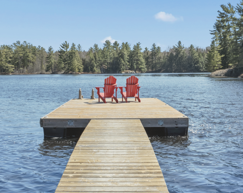 Aerial view of a snowy landscape with a frozen lake featuring small islands and tire tracks, surrounded by snow-covered trees and houses.
