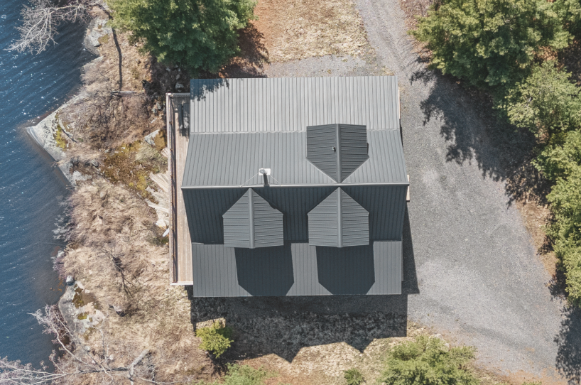 Aerial view of a snowy landscape with a frozen lake featuring small islands and tire tracks, surrounded by snow-covered trees and houses.