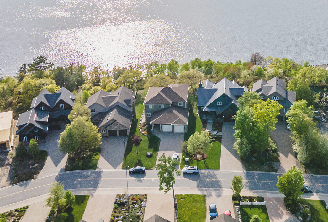 Aerial view of a snowy landscape with a frozen lake featuring small islands and tire tracks, surrounded by snow-covered trees and houses.