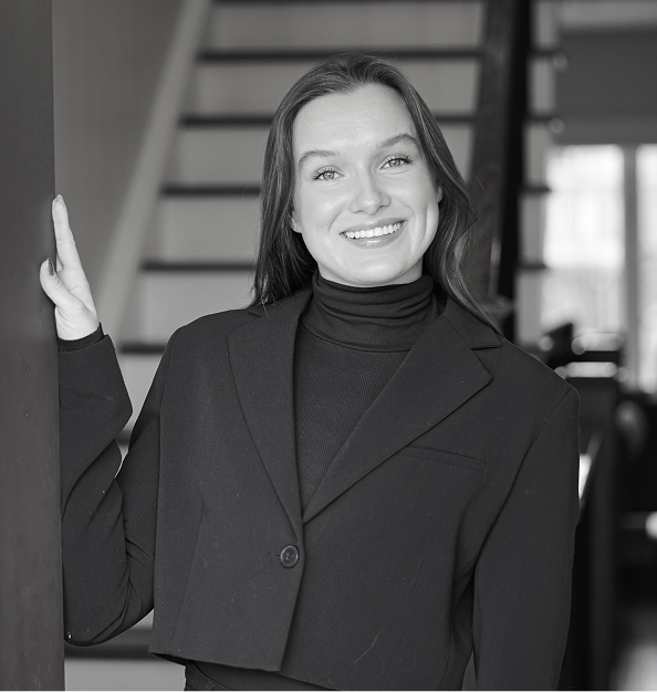 Smiling woman with long blonde hair wearing a black blazer and white top against a light background.