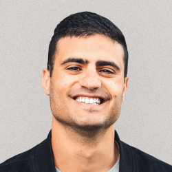 Smiling man with short dark hair wearing a black jacket against a gray background.