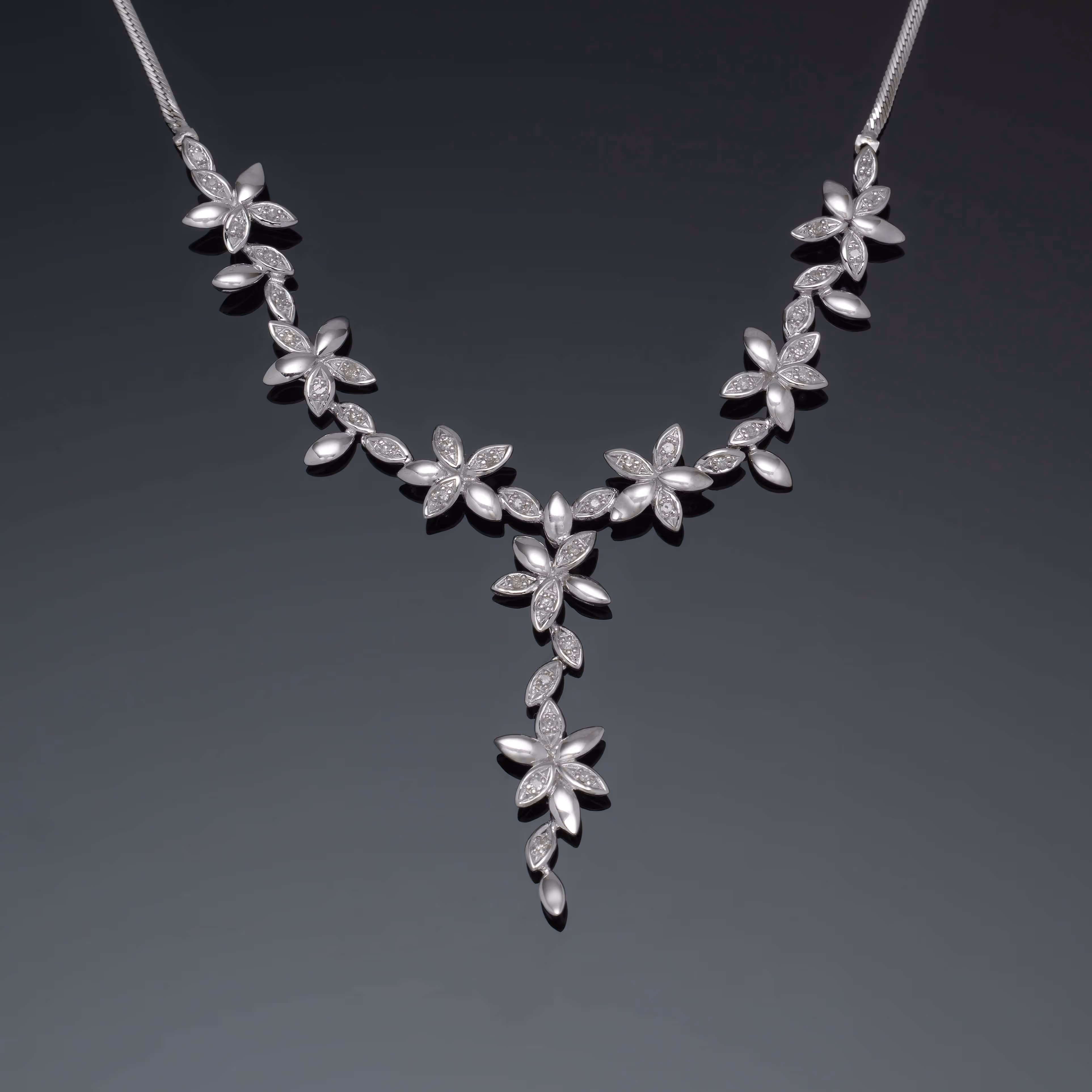 Silver necklace with floral-shaped diamond clusters arranged in a Y pattern on a dark background.