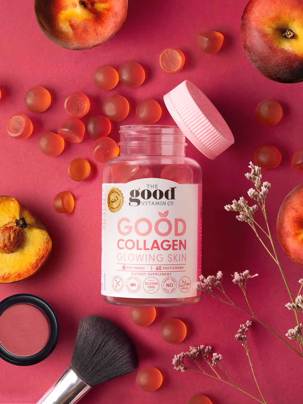 Bottle of Good Collagen peach-flavored gummies with peaches, makeup brush, and flowers on pink background.