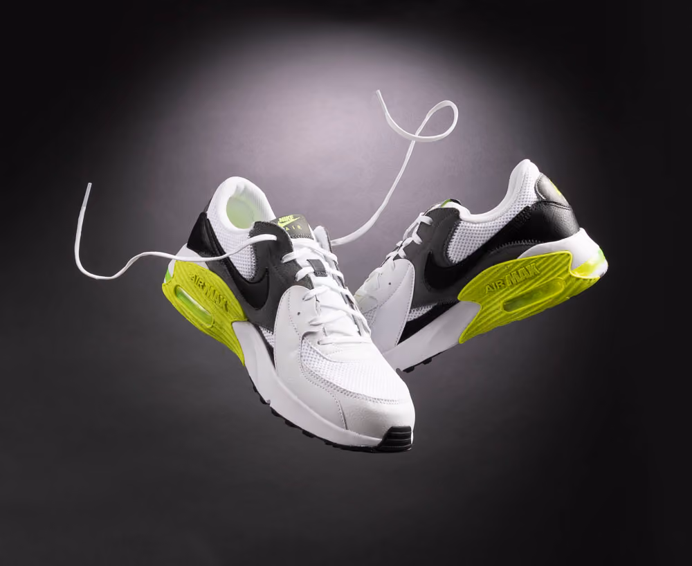 Pair of white Nike Air Max sneakers with black swoosh and neon green heel accents and floating laces.