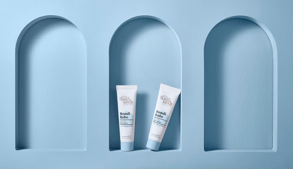 Auckland product photography of Bondi Sands Bondi Babe Purifying Clay Mask tubes styled in an arched alcove set against a soft blue textured background, by Amanda Hughes Photography.